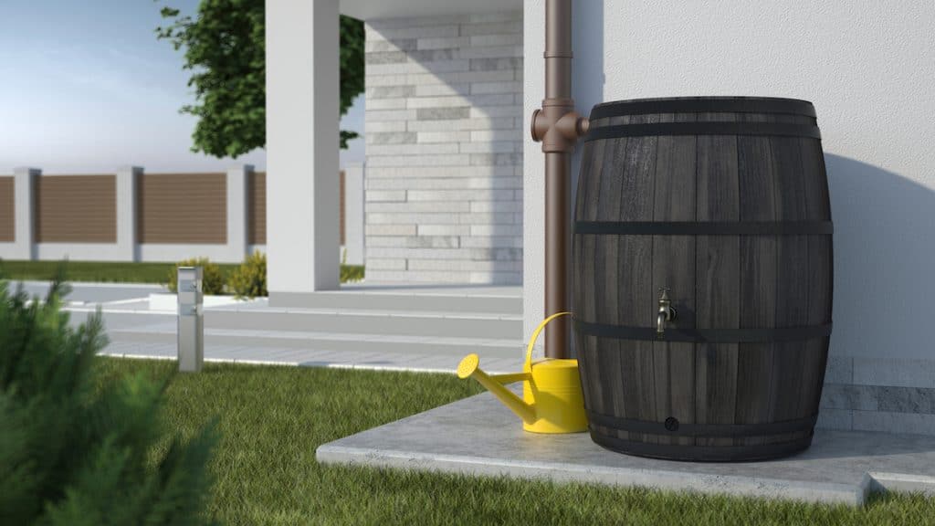 illustration 3D présentant un fût en chène transformé en récupérateur d'eau de pluie installé le long d'un mur d'une maison avec un arrosoir jaune à ses côtés.